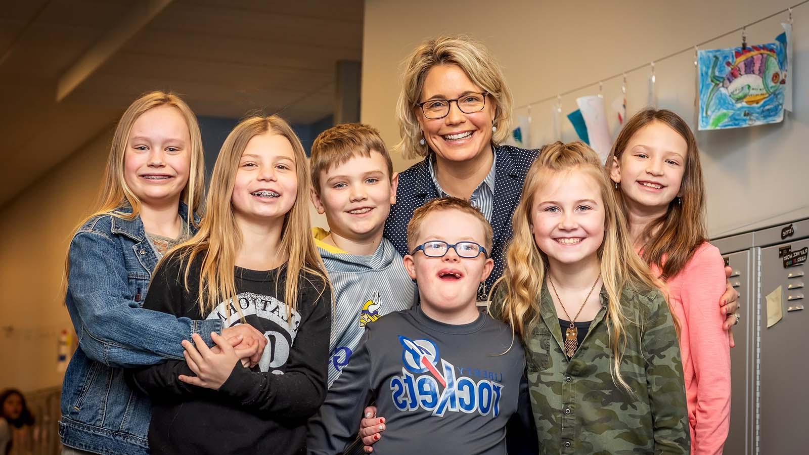 Group of smiling elementary students and teacher in the hallway of a school